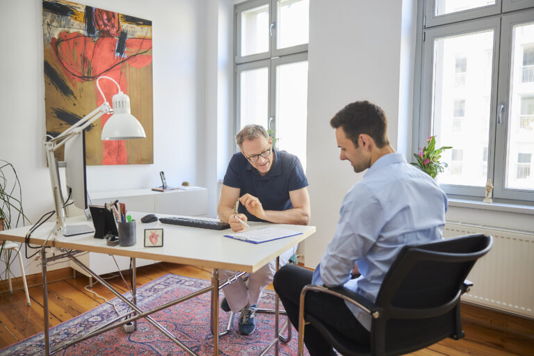 Dr. Moser mit einem Patienten in dem Behandlungszimmer seiner Praxis als Symbolbild für das Thema Angina Pectoris